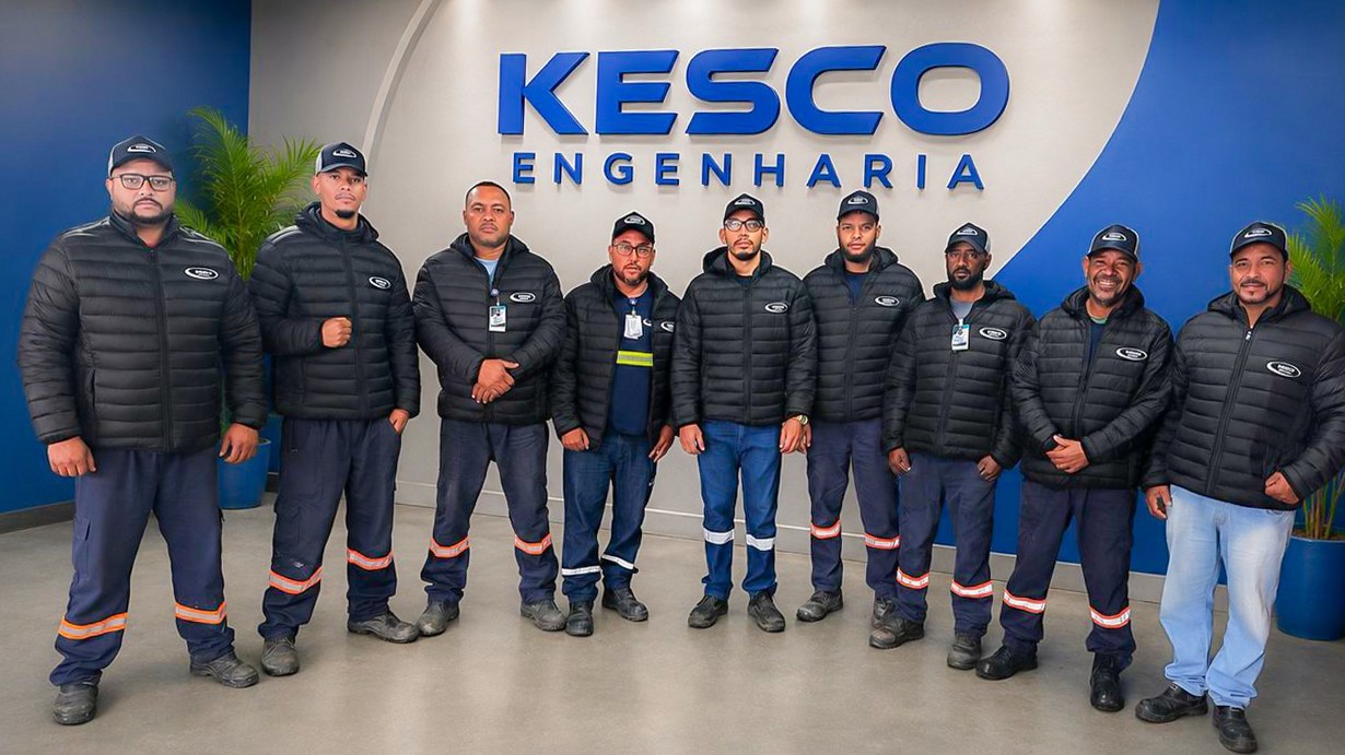Equipe da Kesco reunida na recepção da empresa, diante do letreiro Kesco Engenharia